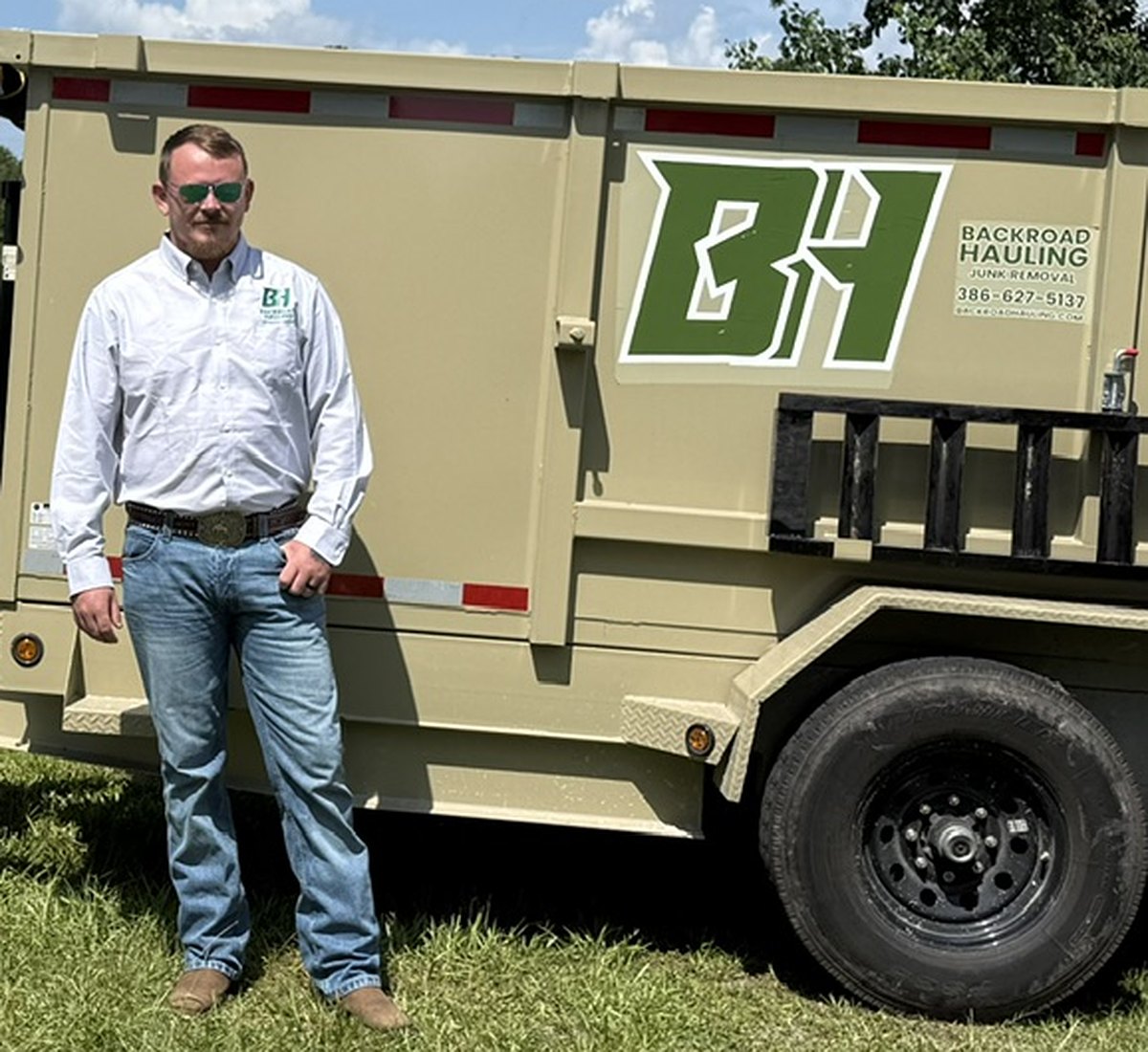 David of Backroad Hauling beside the branded 14-foot dump trailer showing the BH logo and phone number